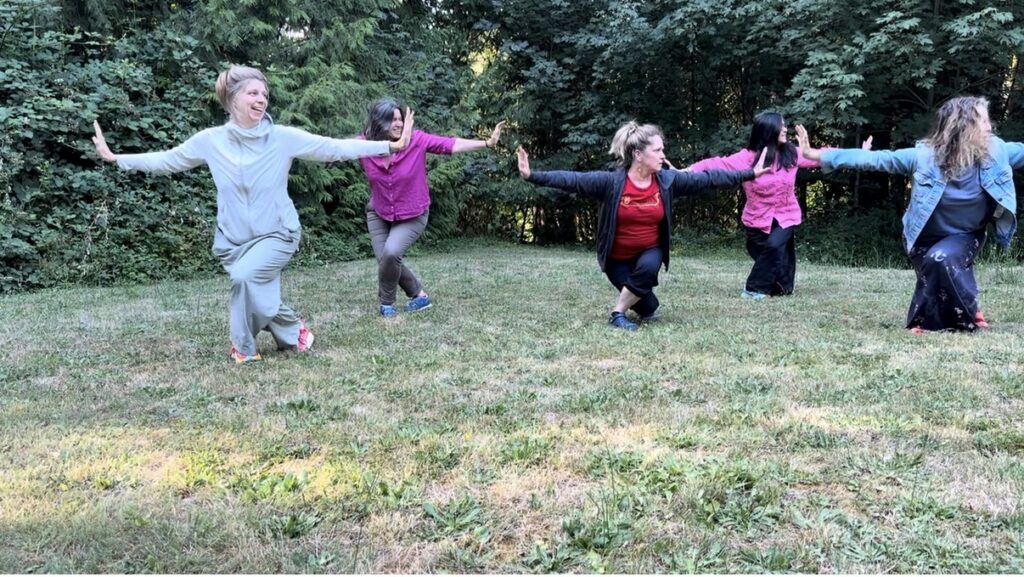 Five women, arms outstretched and knees bent, hold the same pose outdoors.